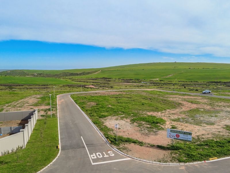 Aerial view of a vacant residential plot in a developed estate, featuring paved roads, boundary walls, and scenic landscape views.