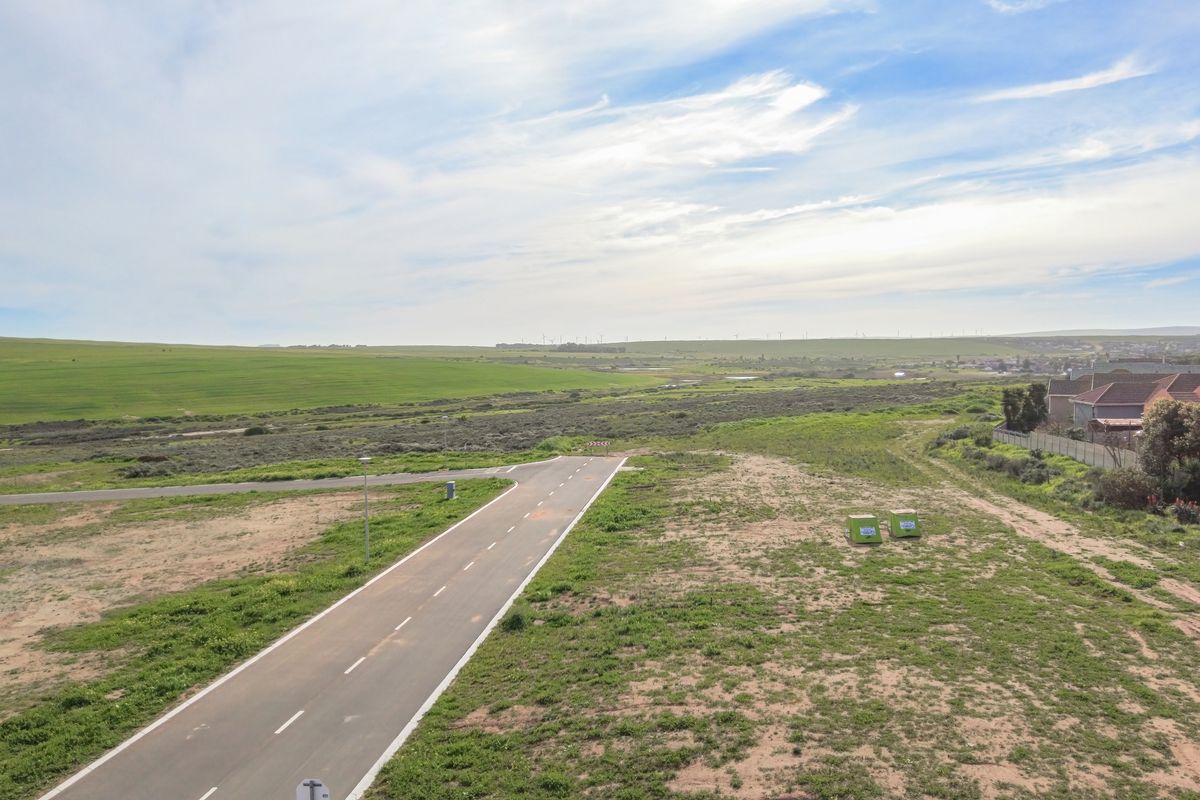 An aerial view of a vacant residential plot featuring a paved access road and surrounding open landscape.