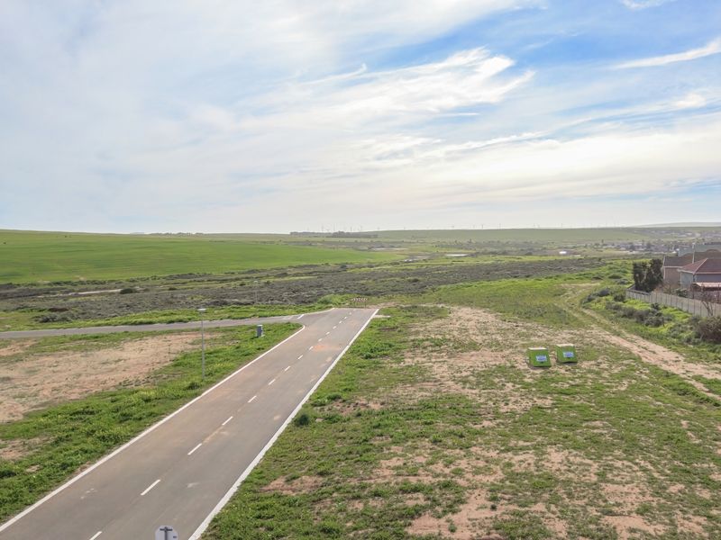 An aerial view of a vacant residential plot featuring a paved access road and surrounding open landscape.