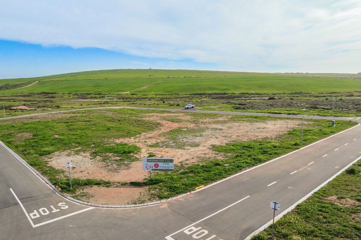 An aerial view of a vacant residential plot situated on a corner, featuring established paved roads and surrounding landscape views.