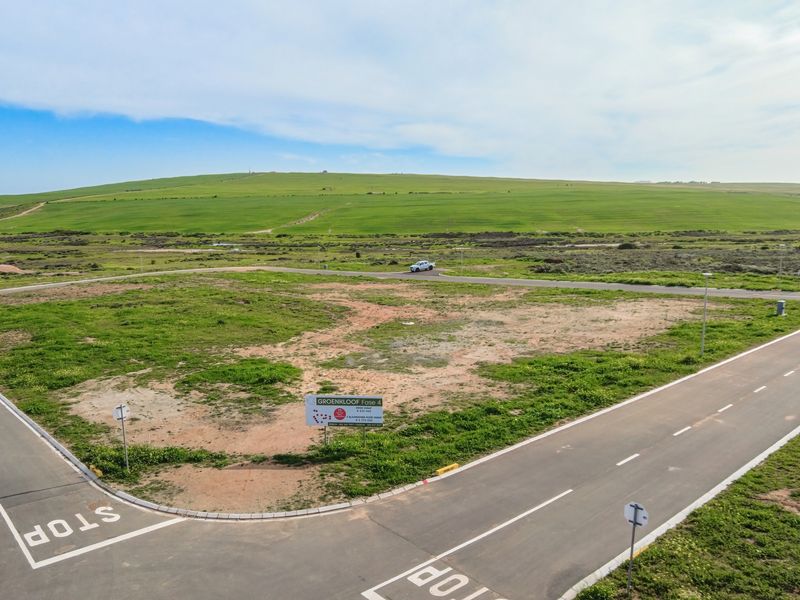 An aerial view of a vacant residential plot situated on a corner, featuring established paved roads and surrounding landscape views.