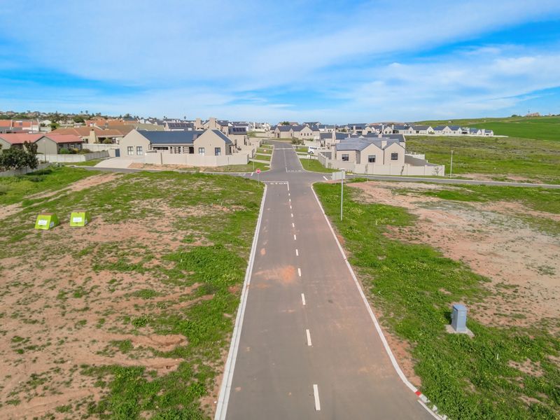 Aerial view of a residential development site featuring paved roads, established street infrastructure, and surrounding vacant land plots.