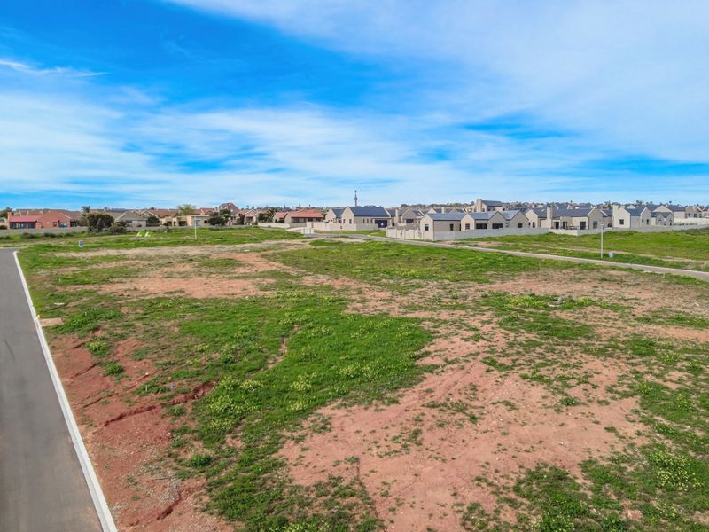 An aerial view of a vacant residential plot situated in a developed neighborhood with established paved road access.