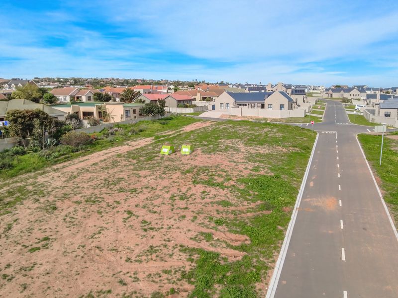 An aerial view of a vacant residential plot situated in a developed suburban estate with paved road access.