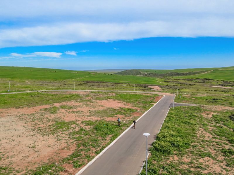 An aerial view of a vacant residential plot featuring a paved road, street lighting, and expansive surrounding landscape.