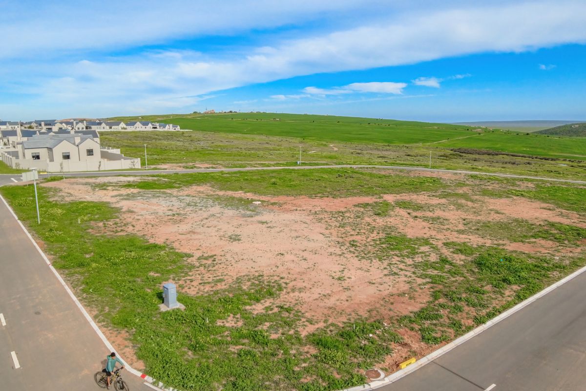 Aerial view of a vacant residential plot situated on a corner, featuring established road infrastructure and surrounding green landscape.