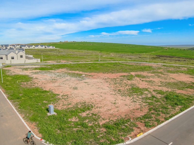 Aerial view of a vacant residential plot situated on a corner, featuring established road infrastructure and surrounding green landscape.