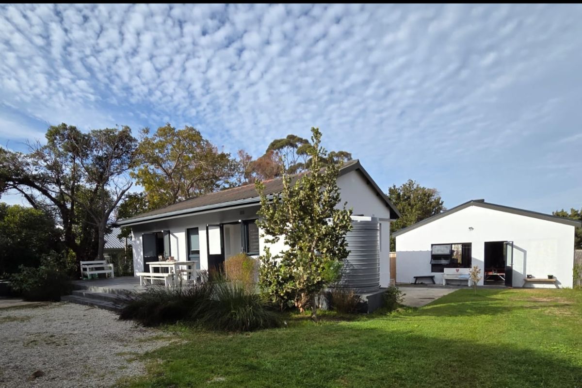 Rear view of the property featuring a white exterior, attached decking, a water tank, and a well-maintained garden area.