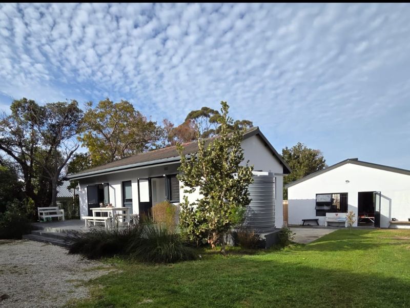 Rear view of the property featuring a white exterior, attached decking, a water tank, and a well-maintained garden area.