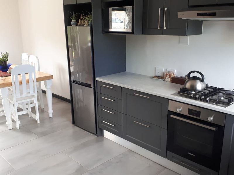 Modern open-plan kitchen featuring dark cabinetry, stone-look countertops, integrated appliances, and tiled flooring, seamlessly flowing into the adjacent dining area.