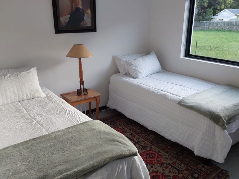 A bright bedroom featuring neutral walls, a large window with a roller blind, and space for two single beds.
