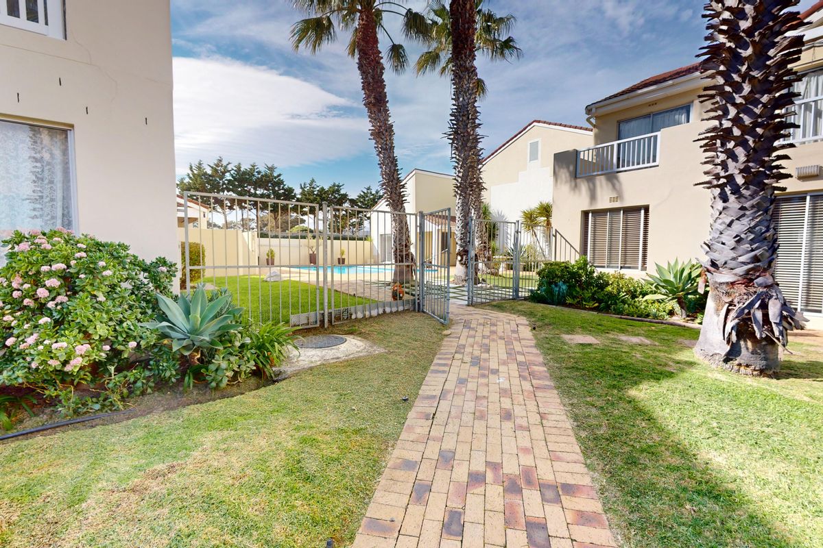 A well-maintained rear garden area featuring a paved walkway, metal fencing, and access to a communal swimming pool and apartment balcony.