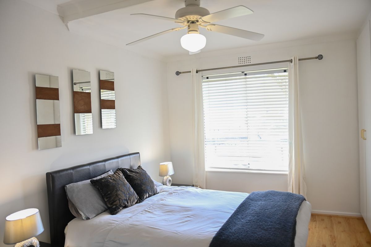 A well-lit bedroom featuring timber flooring, a ceiling fan, and a built-in wardrobe, offering a comfortable and functional living space.