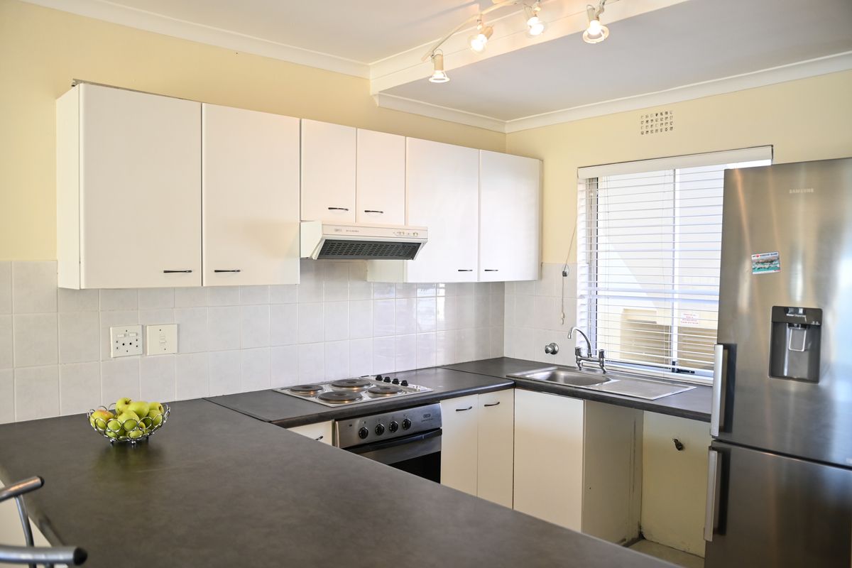 A functional kitchen featuring white cabinetry, dark laminate countertops, a built-in electric hob and oven, and a stainless steel sink with tiled backsplash.