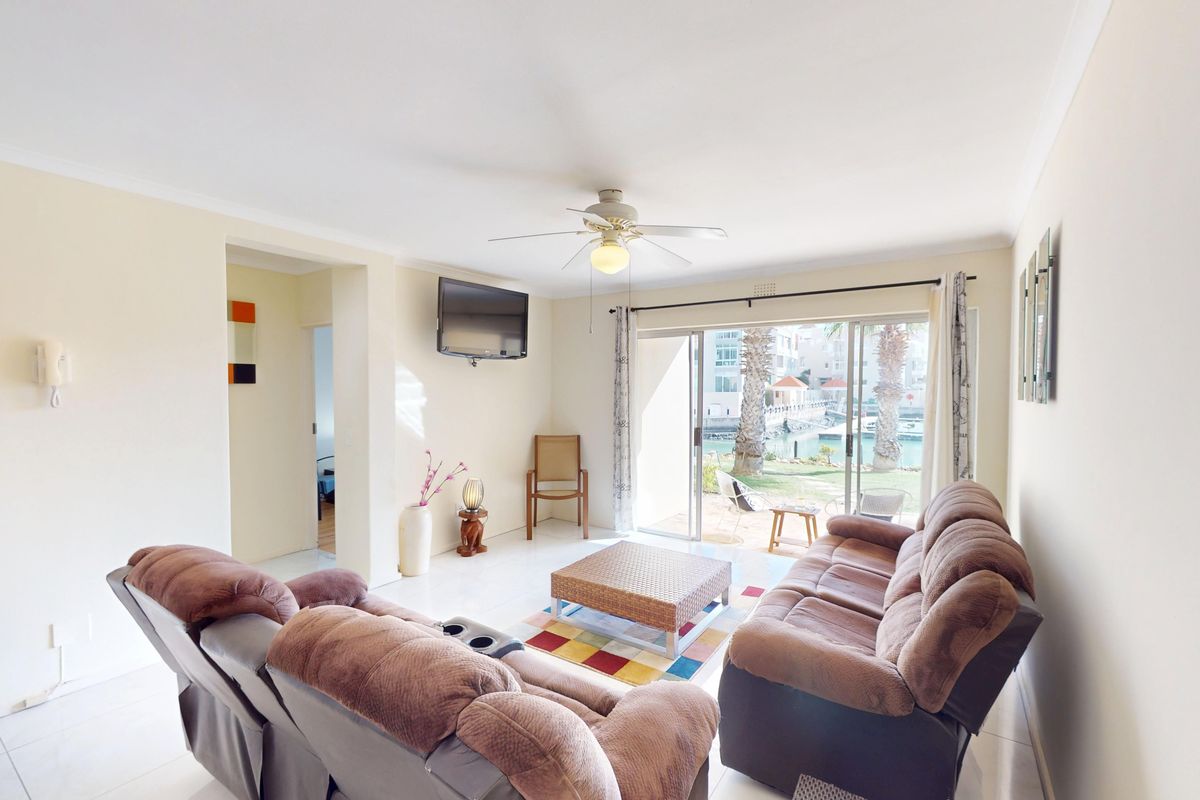 A bright living room featuring tiled flooring, a ceiling fan, and large sliding glass doors that provide access to an outdoor patio area.