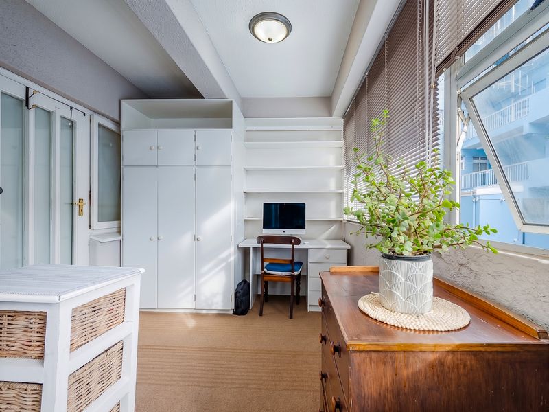 A functional home office space featuring built-in cabinetry, integrated desk, and shelving, with large windows and venetian blinds providing natural light.