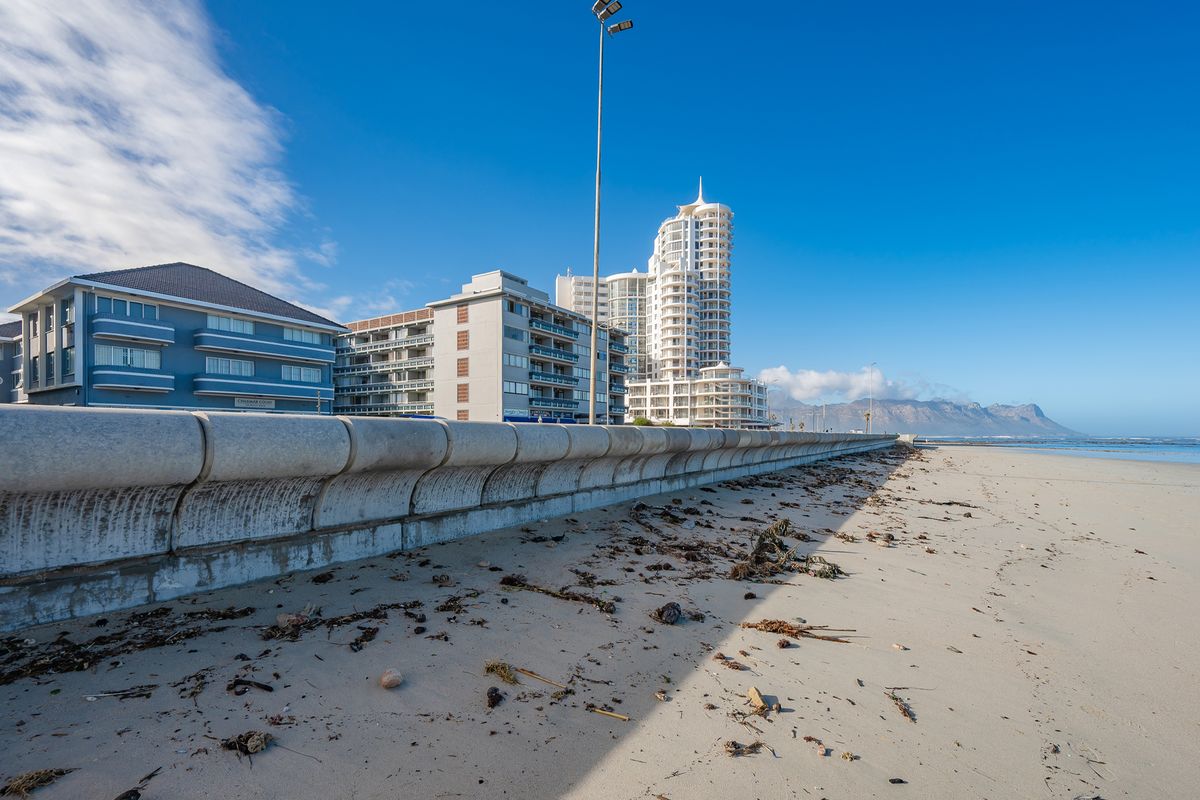 A view of the concrete sea wall and coastal apartment buildings along the beach, showcasing the property's proximity to the ocean.