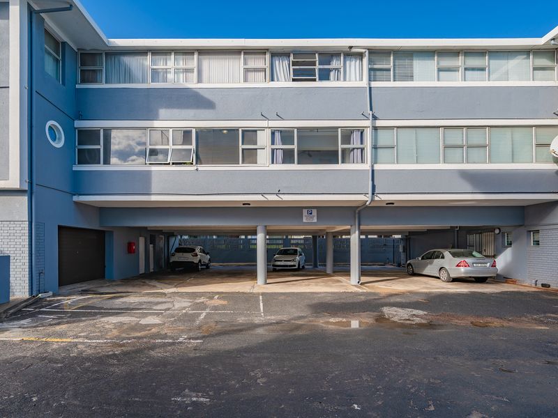 Front elevation of an apartment building featuring covered ground-level parking bays and multiple residential units with sliding windows.