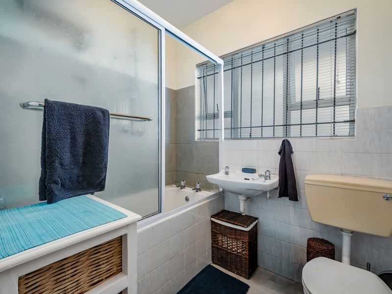 A functional bathroom featuring a bathtub with a shower screen, a pedestal basin, and a toilet, finished with tiled walls and security window bars.