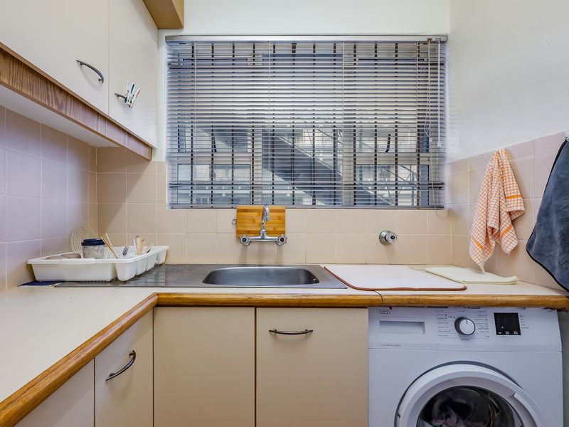A functional laundry area featuring built-in cabinetry, a stainless steel sink, tiled backsplash, and space for a washing machine.