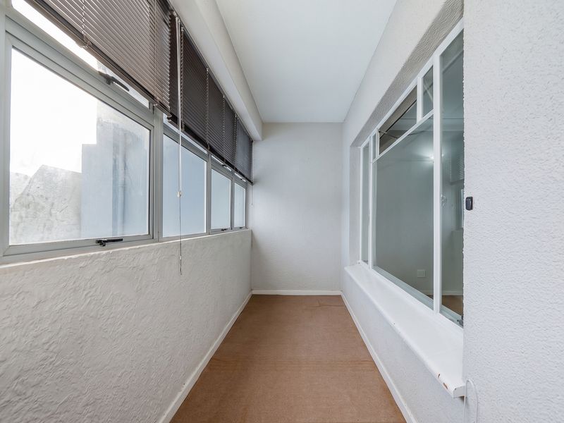 An enclosed balcony or sunroom featuring aluminium window frames, venetian blinds, and a neutral textured wall finish, offering a versatile additional living space.