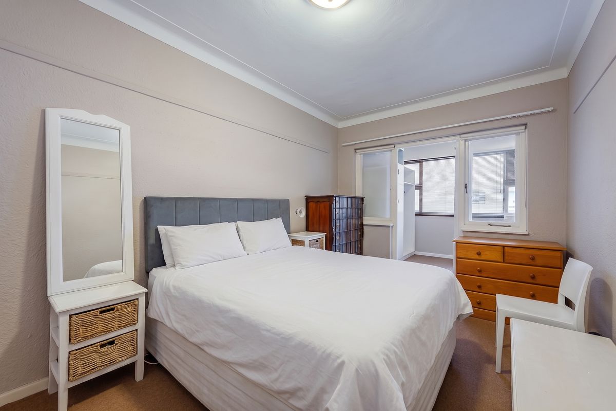 A well-lit bedroom featuring neutral wall tones, carpeted flooring, and a built-in cupboard with access to an adjoining space.