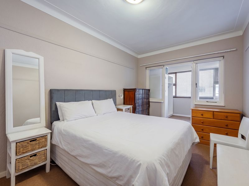 A well-lit bedroom featuring neutral wall tones, carpeted flooring, and a built-in cupboard with access to an adjoining space.