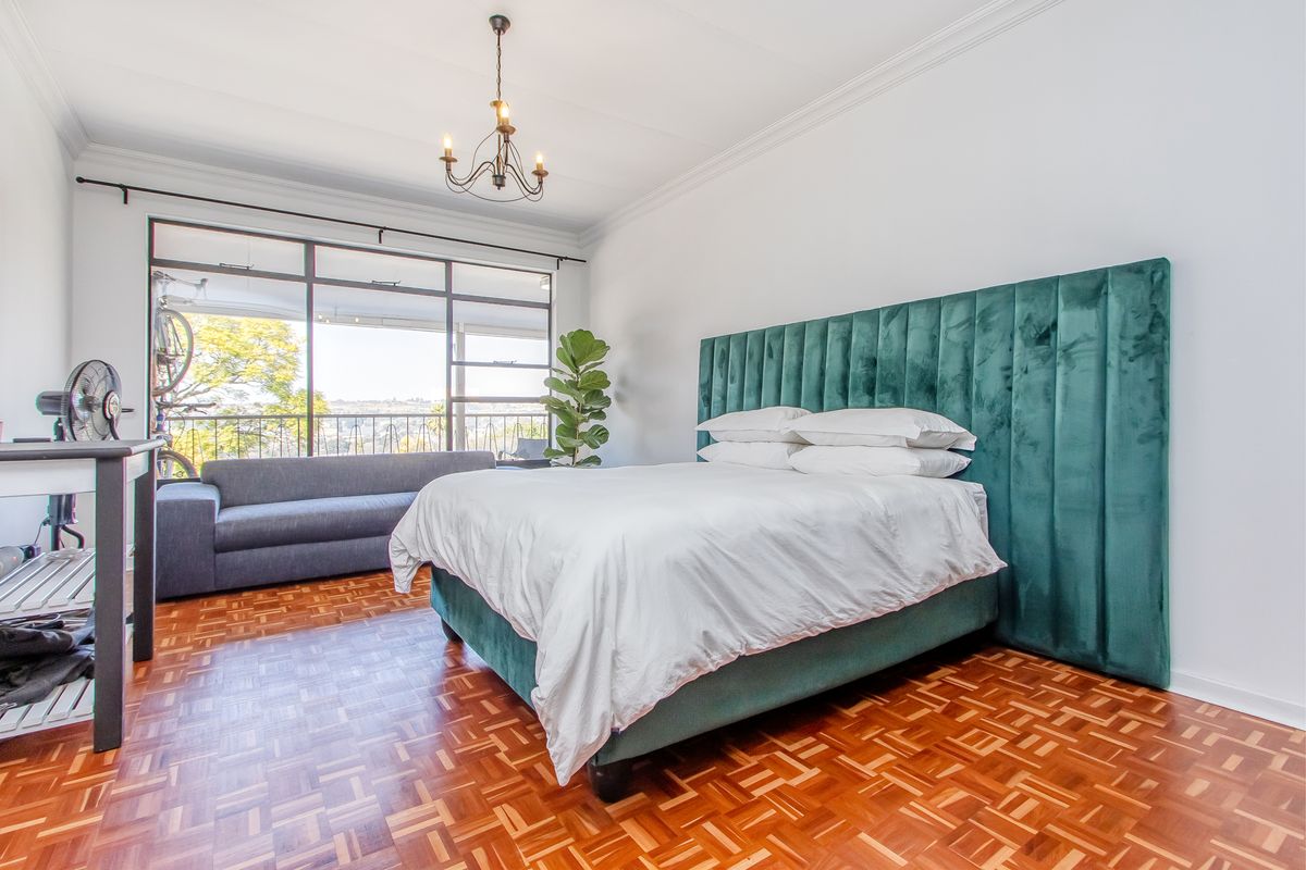 Spacious bedroom featuring classic parquet flooring, elegant crown molding, and large steel-framed windows that provide ample natural light and scenic views.