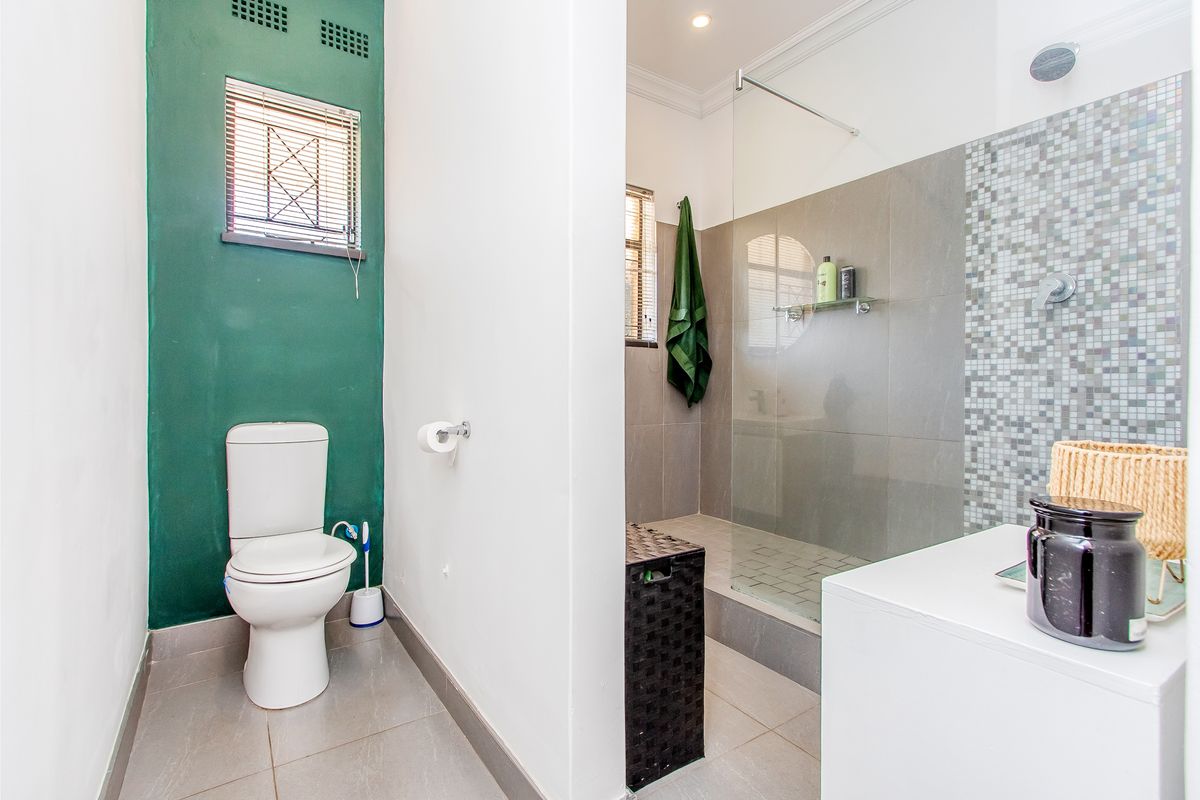 Modern bathroom featuring a walk-in shower with glass screen, mosaic tile accents, and a separate toilet area with green feature wall.