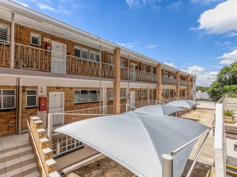 Exterior view of a multi-story apartment complex featuring brick facade, metal balustrades, and covered parking shade sails.