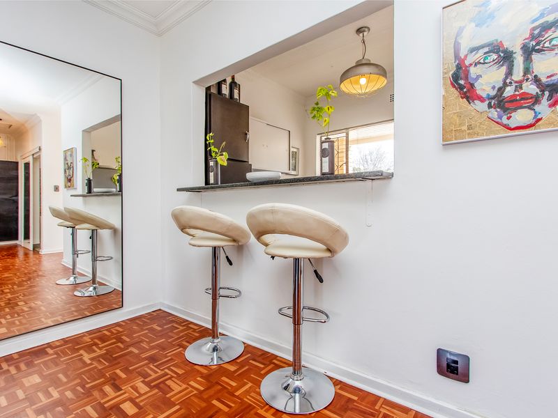 Open plan living area featuring classic parquet flooring, a breakfast bar pass-through to the kitchen, and a large wall-mounted mirror.