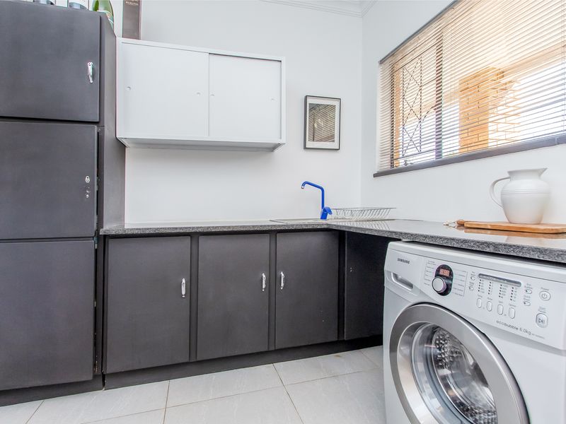 A functional laundry room featuring dark built-in cabinetry, granite countertops, a stainless steel sink, and tiled flooring with natural light from a window.