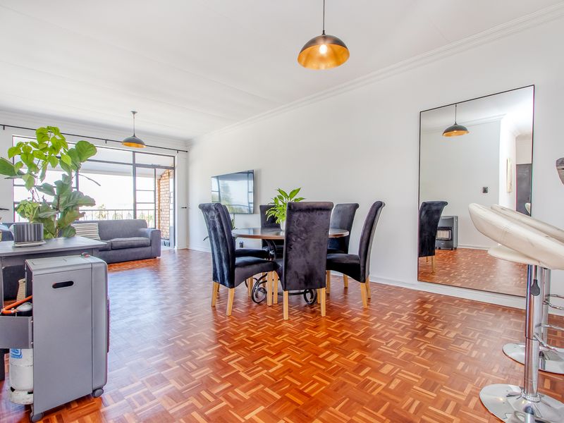 Spacious open-plan living and dining area featuring classic parquet flooring, crown molding, and a large wall mirror, with direct access to a balcony.