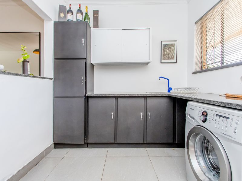 A functional laundry area featuring built-in dark cabinetry, granite countertops, a sink, and tiled flooring, providing efficient utility space within the apartment.
