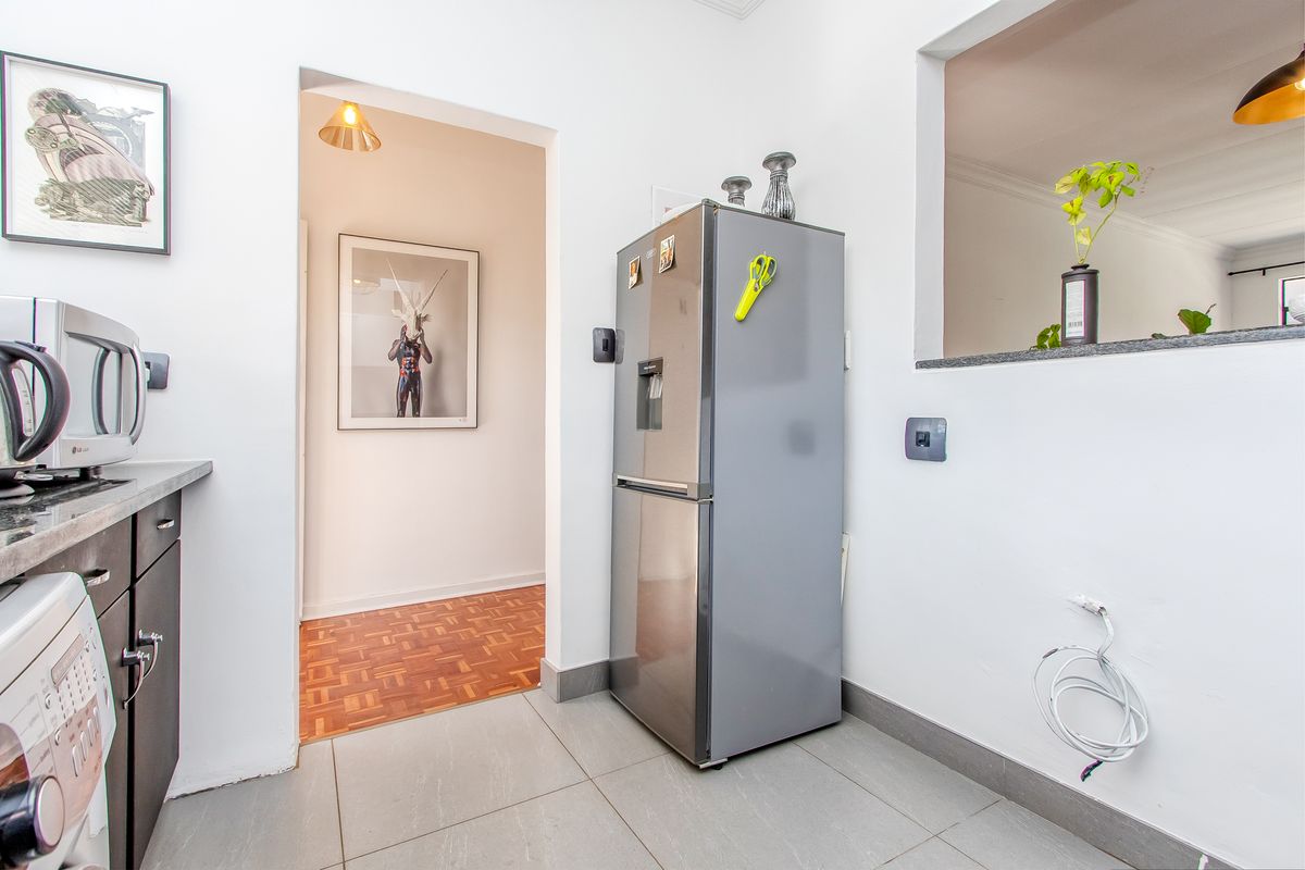 A functional kitchen area featuring tiled flooring, built-in cabinetry with stone countertops, and a convenient pass-through window connecting to the adjacent living space.