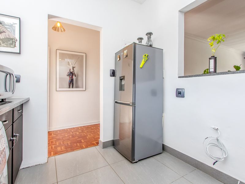 A functional kitchen area featuring tiled flooring, built-in cabinetry with stone countertops, and a convenient pass-through window connecting to the adjacent living space.