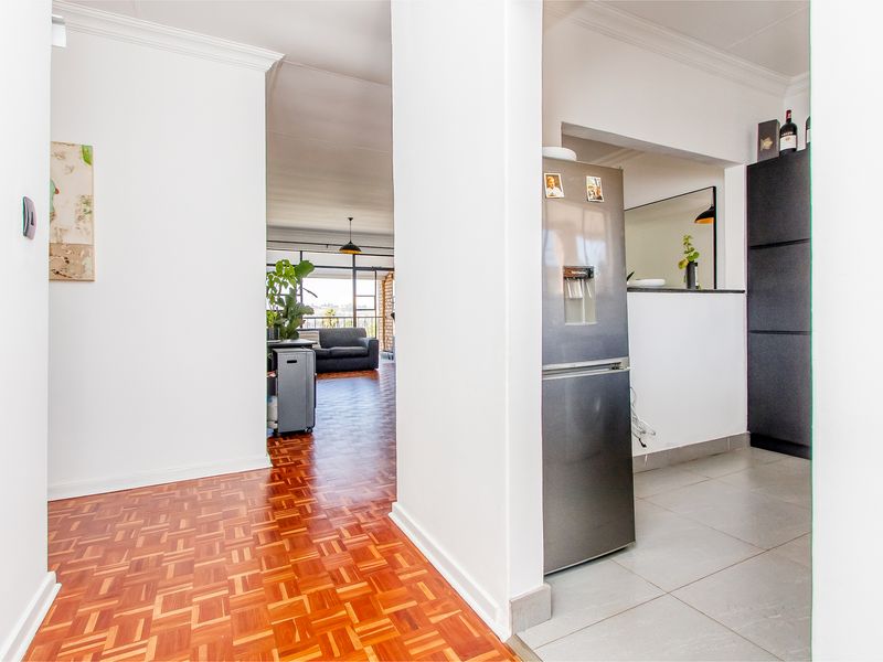 Open plan apartment interior featuring a transition between parquet and tiled flooring, with a pass-through window connecting the kitchen and living areas.