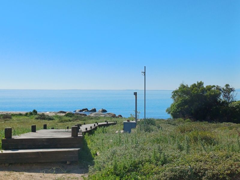 A scenic view of the coastline featuring a wooden boardwalk leading towards the ocean, surrounded by natural coastal vegetation.
