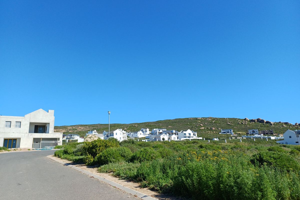 A street-level view of a residential area featuring an asphalt road, curb infrastructure, and surrounding coastal landscape with nearby homes.