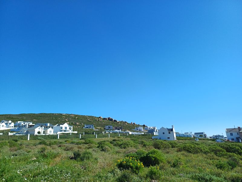 A scenic view of a coastal residential area featuring natural vegetation and surrounding hillside landscape.