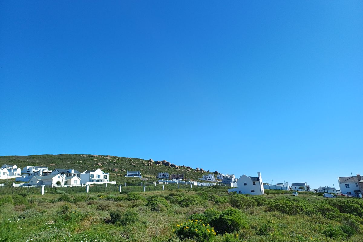 A scenic view of a coastal residential area featuring natural vegetation and surrounding hillside landscape.