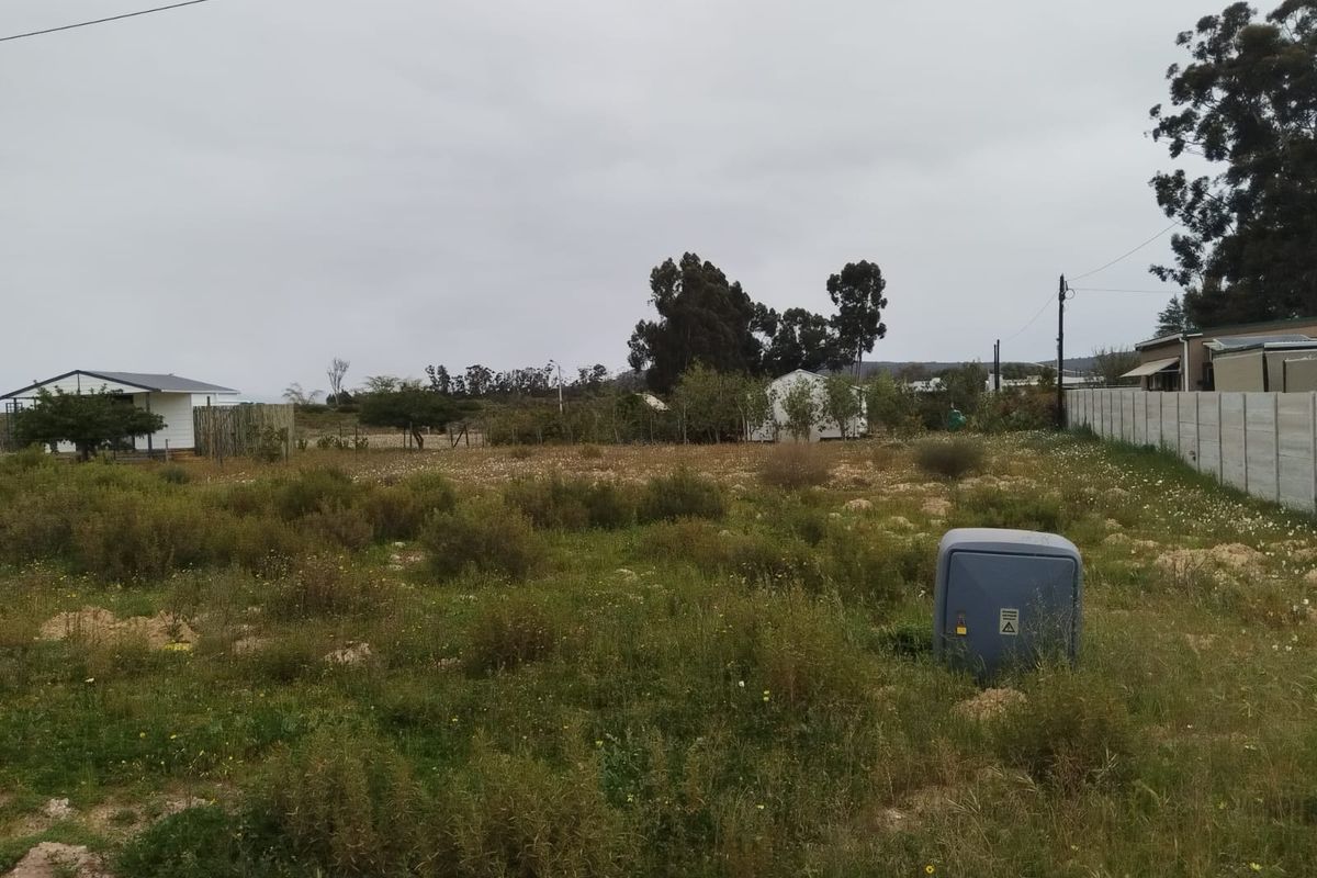 A vacant residential plot featuring natural vegetation, a precast concrete boundary wall, and an existing electrical utility connection point.