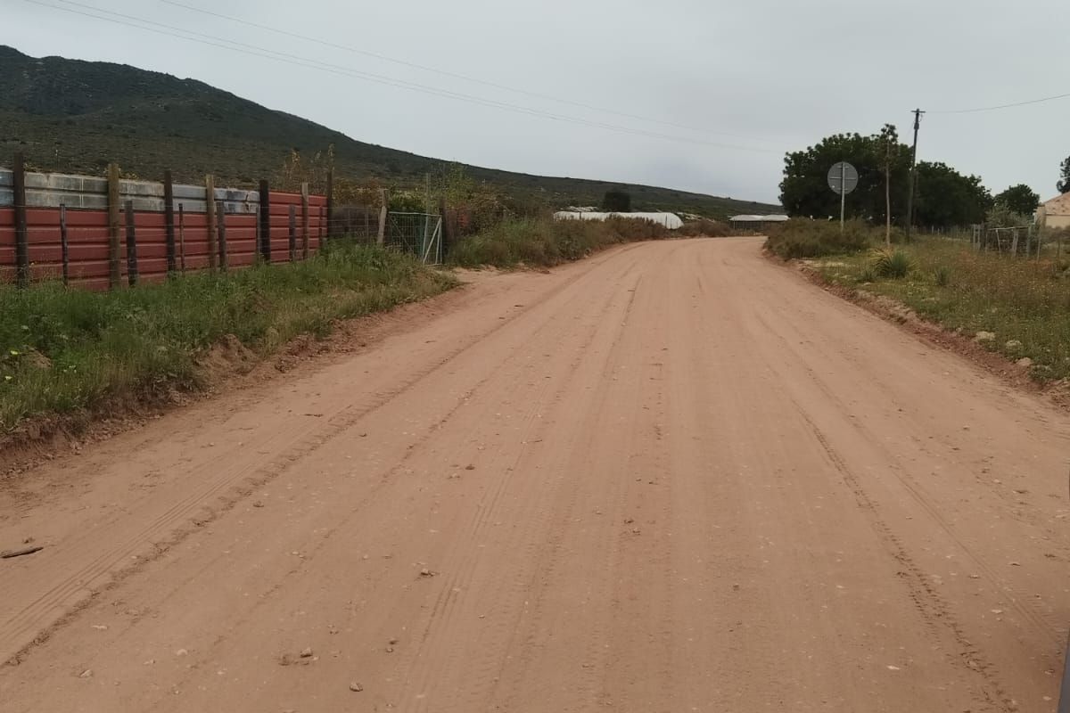 A view of an unpaved dirt road providing access to the property, featuring perimeter fencing and surrounding rural landscape.