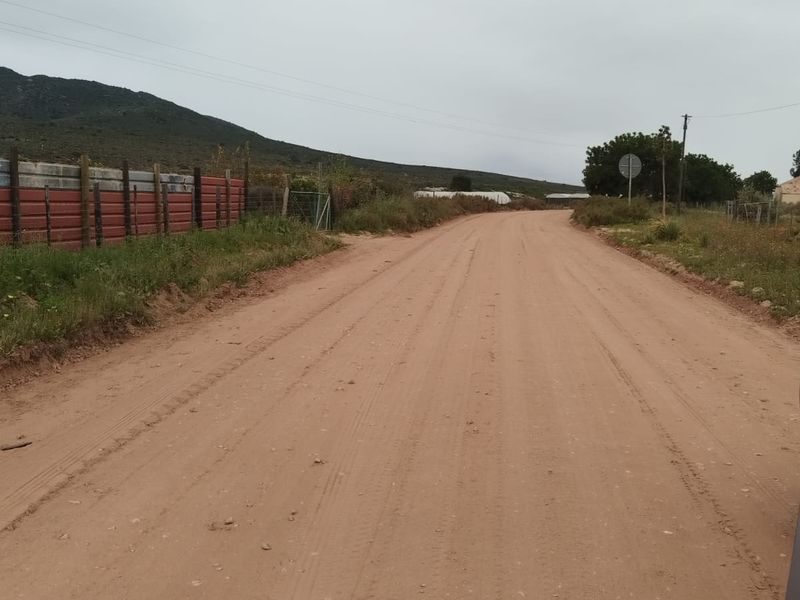 A view of an unpaved dirt road providing access to the property, featuring perimeter fencing and surrounding rural landscape.