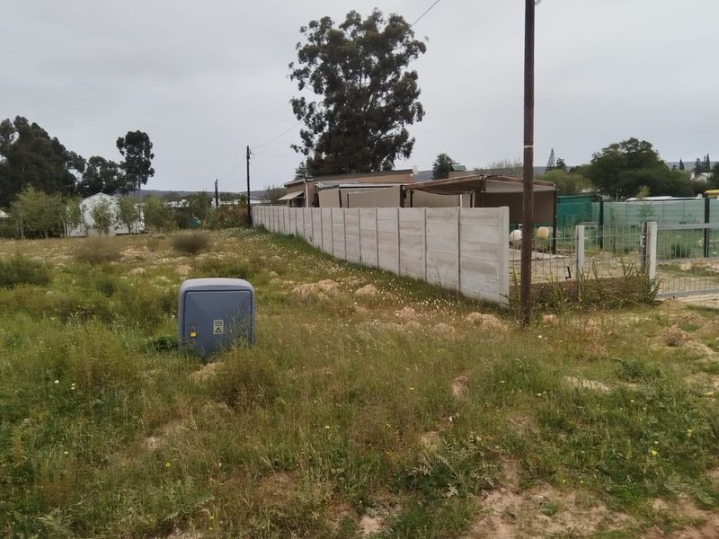 Vacant residential land featuring a precast concrete boundary wall, utility connection point, and established perimeter fencing.