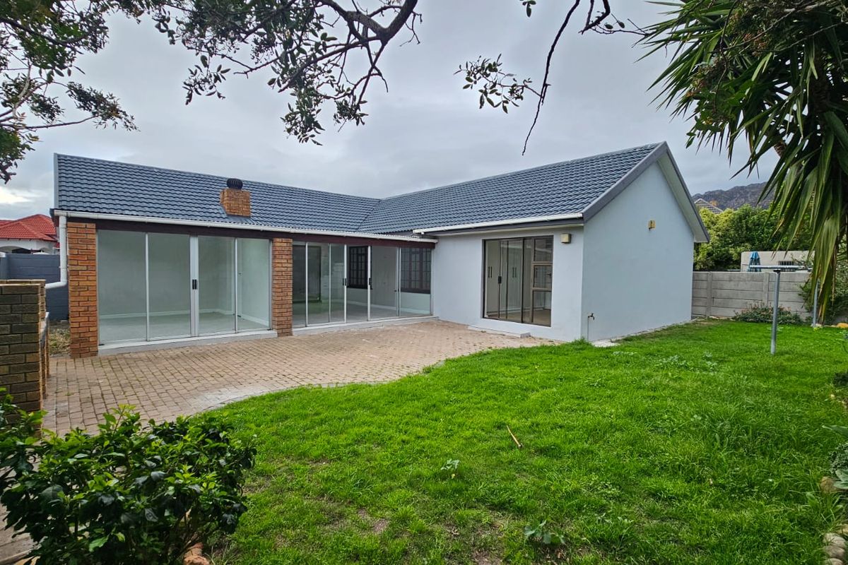 Rear view of the property featuring a paved patio area, sliding glass doors, and a private garden with a built-in brick braai.