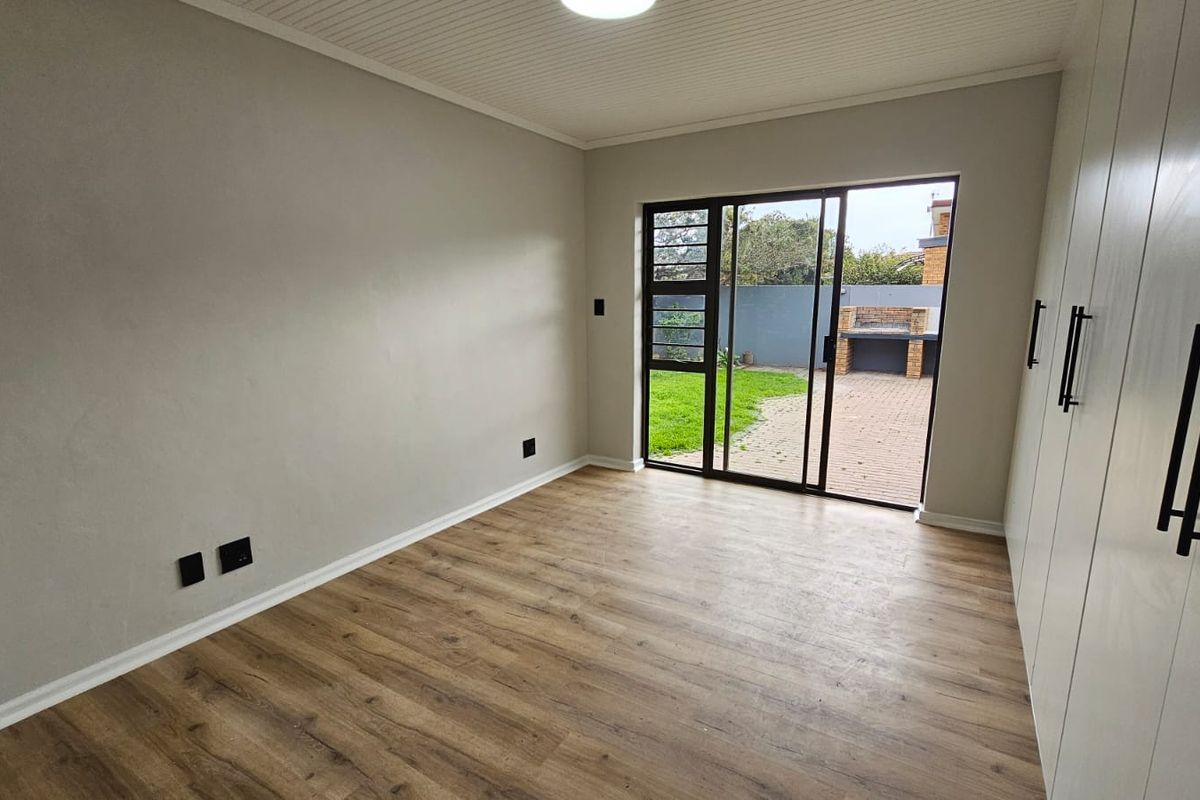 A bright, empty bedroom featuring modern laminate flooring, built-in cupboards, and a sliding glass door providing direct access to the rear garden and patio.