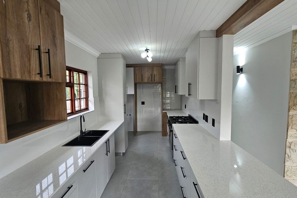 Modern kitchen featuring sleek white cabinetry, wood-tone accents, quartz countertops, a gas hob, and a striking stone feature wall.