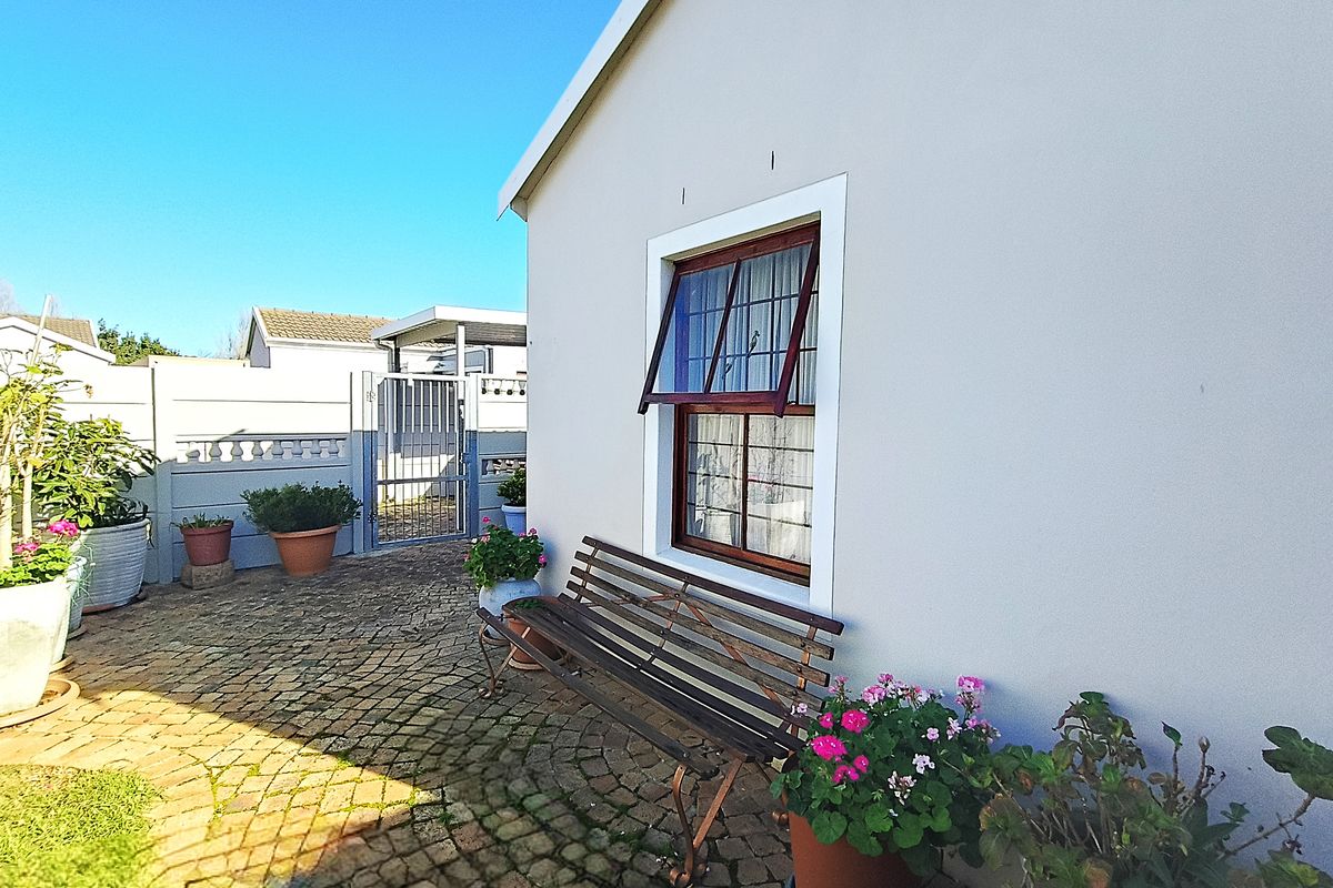 A well-maintained rear exterior area featuring cobblestone paving, a secure boundary wall with a metal gate, and a classic timber-framed window.