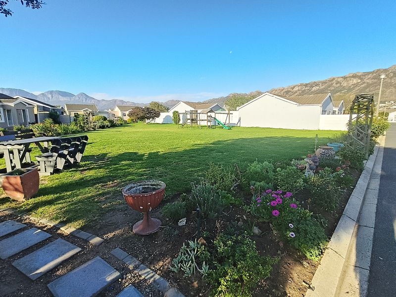 A spacious, well-maintained residential garden featuring a large lawn, established flower beds, and paved pathways with scenic mountain views.